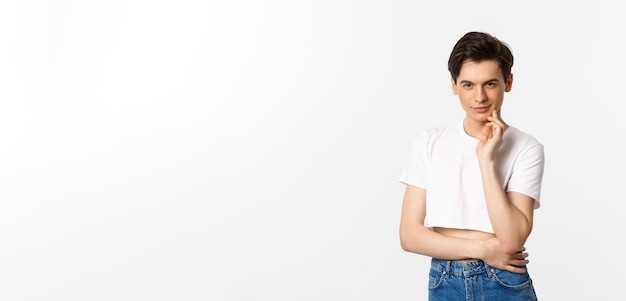 Thoughtful young queer man wearing crop top smiling and looking at camera cunning having an idea sta