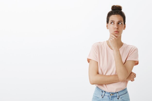 Thoughtful young stylish woman posing against the white wall