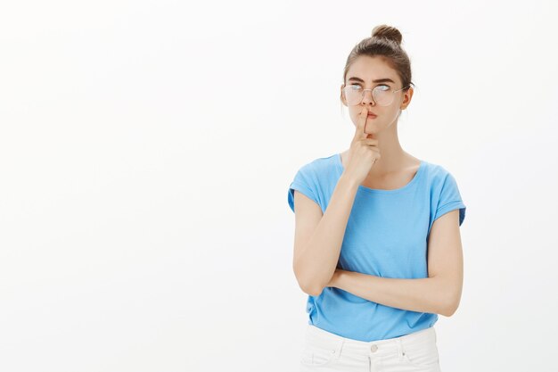 Thoughtful young woman in glasses making plan, thinking, feeling indecisive