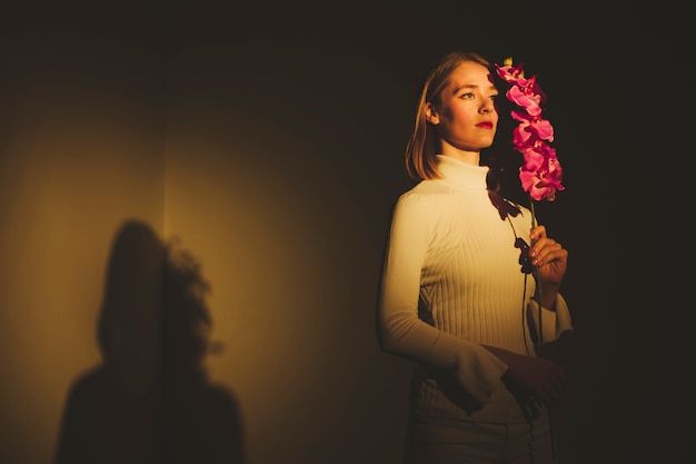 Thoughtful young woman holding pink flower 