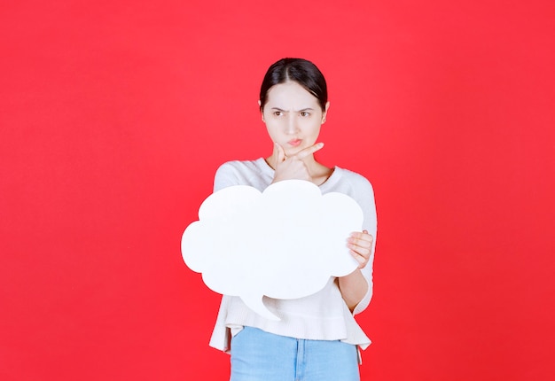 Thoughtful young woman holding speech bubble with a cloud shape