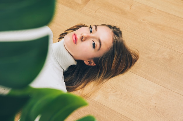 Thoughtful young woman lying on floor near plant