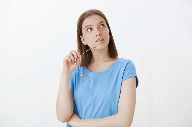 Thoughtful young woman take-off glasses, looking upper right corner, making choice