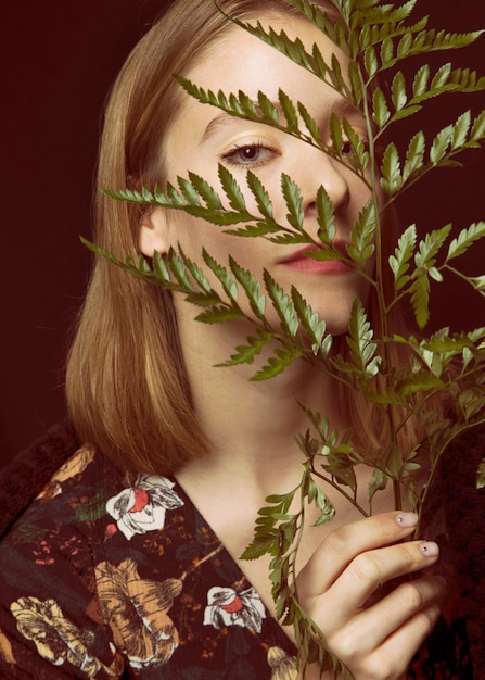 Thoughtful young woman with green plant branch