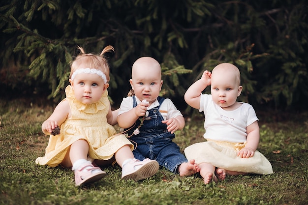 庭のカメラを見ながら春服を着た3人の愛らしい素敵な赤ちゃん。幸せな子供時代の概念