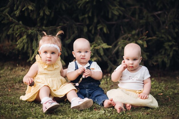 庭のカメラを見ながら春服を着た3人の愛らしい素敵な赤ちゃん。幸せな子供時代の概念