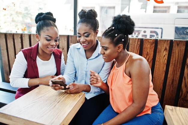Three african american girls sitting on the table of caffe and looking on mobile phone