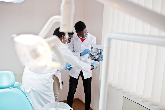 Three african american male doctors working discussing with colleagues in clinic and point on xray skull