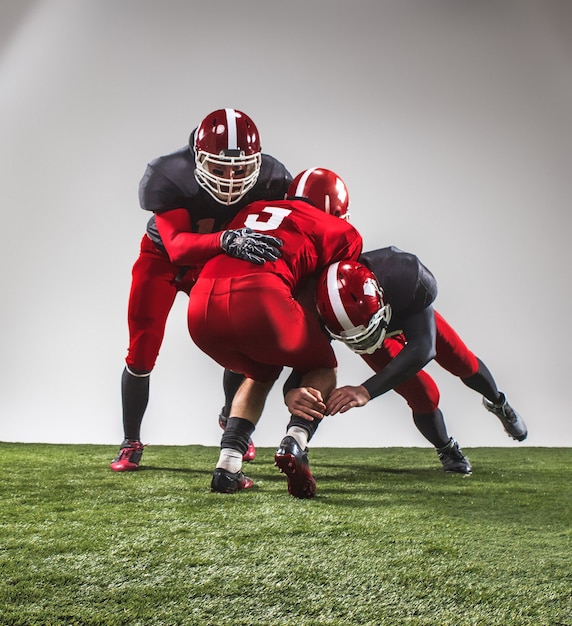 The three american football players in action on green grass and gray background.