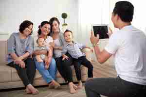 무료 사진 어린 소년과 아기가 태블릿에 사진을 찍고 소파와 남자에 앉아 세 아시아 숙녀