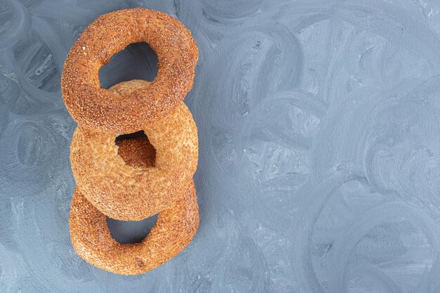 Three bagels coated with sesame lined up on marble table.