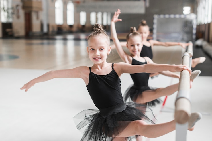 Free Photo three ballerina girls in black tutu stretching their legs on bar