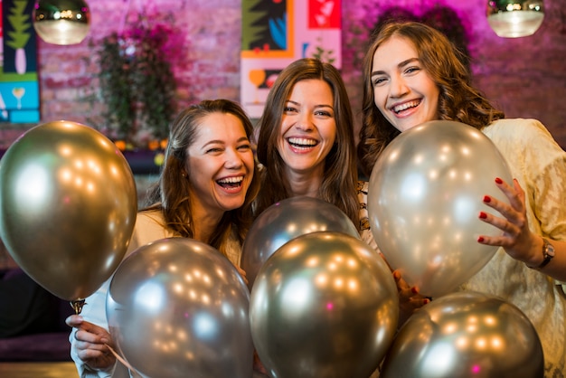 Three beautiful smiling friends holding silver balloons enjoying in party