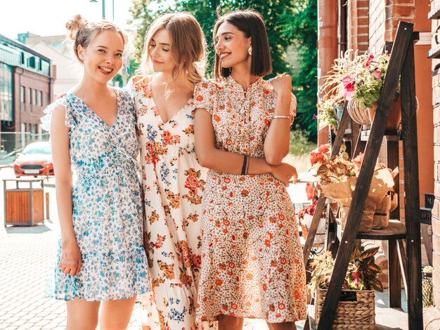 Three beautiful smiling girls in trendy summer sundress posing on the street