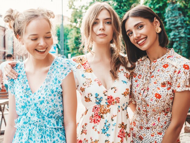 Three beautiful smiling girls in trendy summer sundress posing on the street