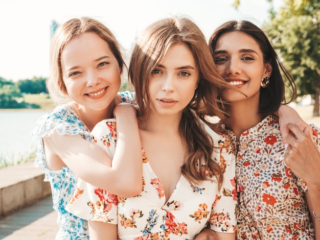 Three beautiful smiling girls in trendy summer sundress posing on the street