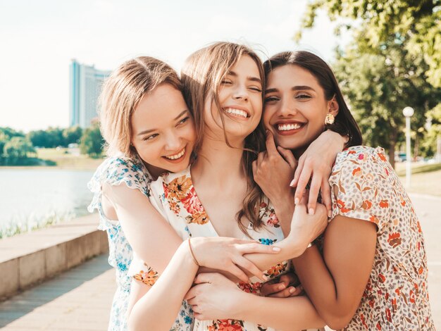 Three beautiful smiling girls in trendy summer sundress posing on the street