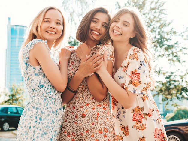 Free photo three beautiful smiling girls in trendy summer sundress posing on the street