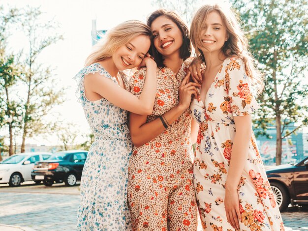 Three beautiful smiling girls in trendy summer sundress posing on the street