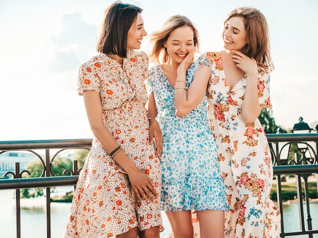 Три красивые улыбающиеся девушки в модном летнем сарафане позируют на улице