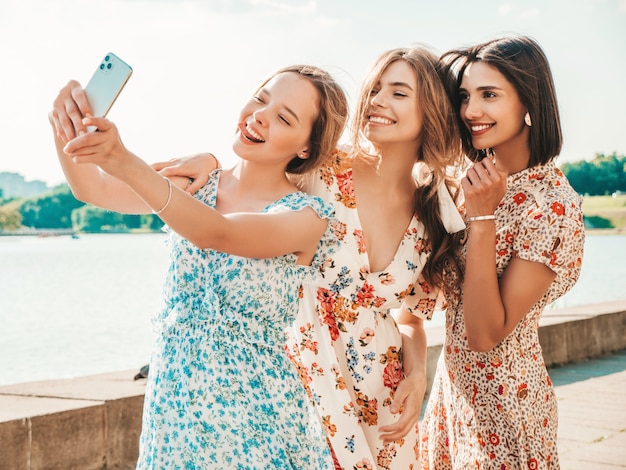 Tre belle ragazze sorridenti in prendisole alla moda estate prendendo selfie