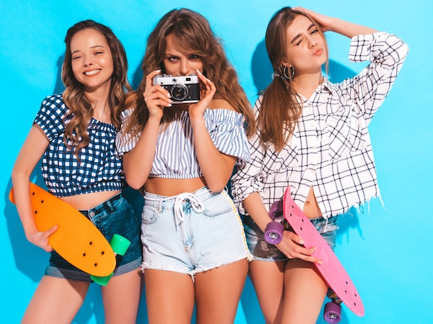 Three beautiful stylish smiling girls with colorful penny skateboards. women in summer. taking pictures on retro photo camera