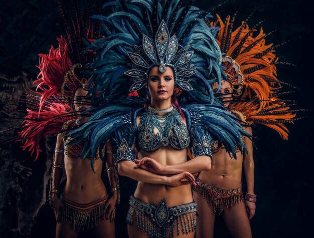 Three beautiful young womans in traditional brasilian carnaval costumes are posing for photographer at studio.