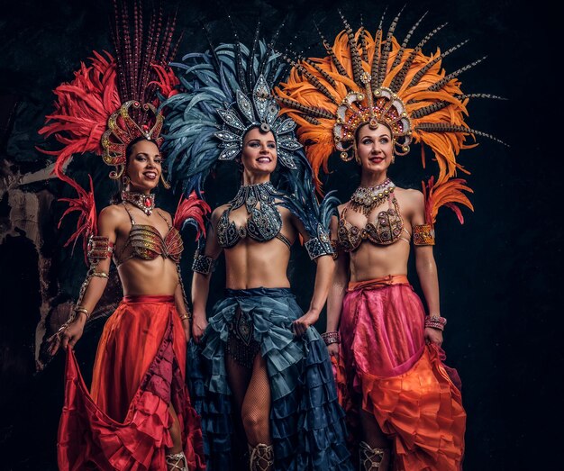 Three beautiful young womans in traditional brasilian carnaval costumes are posing for photographer at studio.