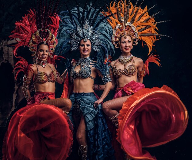 Three beautiful young womans in traditional brasilian carnaval costumes are posing for photographer at studio.