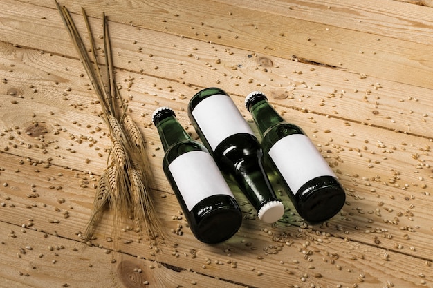 Three beer bottles and ears of wheat on wooden background