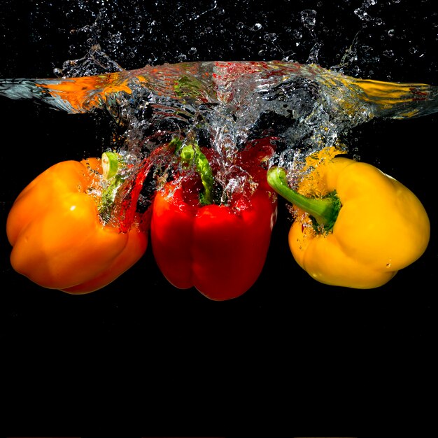 Three bell peppers falling into the splash water