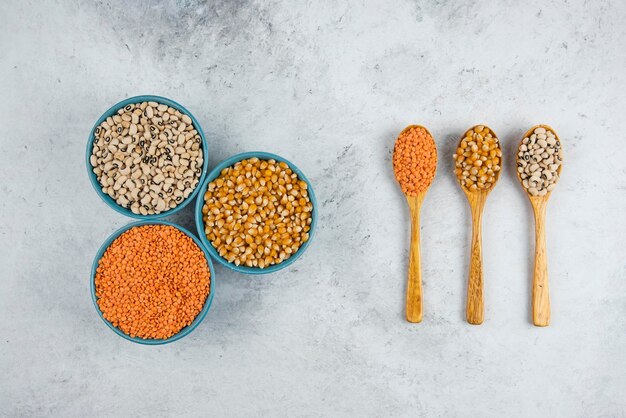 Three blue bowls full of raw beans and wooden spoons.