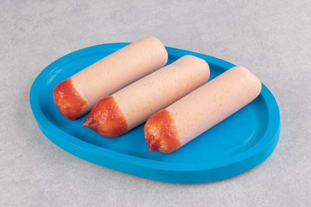 Three boiled sausages with ketchup on blue plate.