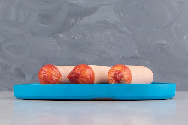 Бесплатное фото Три вареные колбаски с кетчупом на синей тарелке.