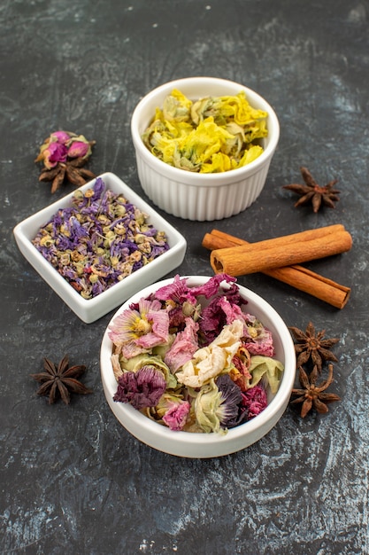 Three bowls of dry flower and cinnamon sticks on grey ground