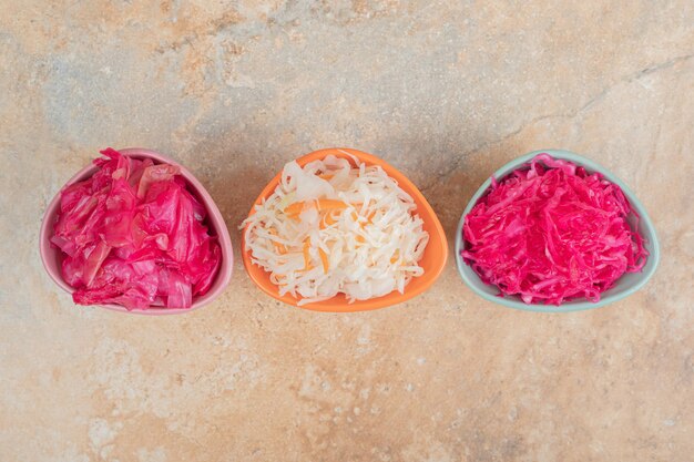 Three bowls of red and white sauerkraut on marble surface.