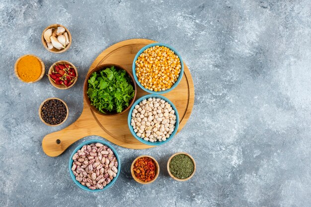 Three bowls of various beans and corns with spices on wooden board.