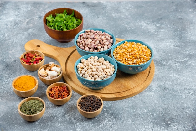 Three bowls of various beans and corns with spices on wooden board.