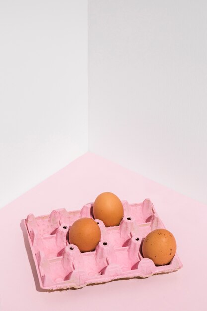 テーブルの上のピンクのラックに3つの茶色の卵