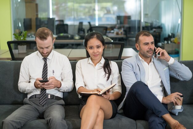 Three business people sitting on sofa and having coffee break