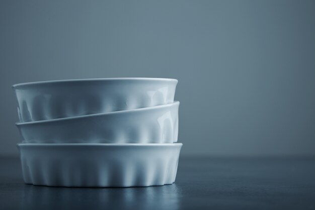 Three ceramic white bowls isolated on side of blue rustic table and grey