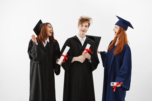 Three cheerful graduates smiling speaking fooling holding diplomas.