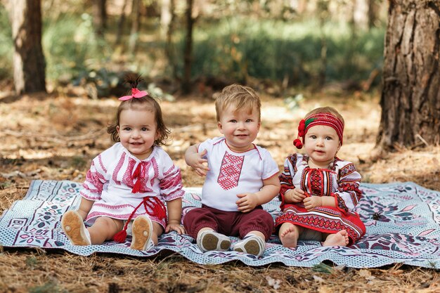 伝統的なウクライナのシャツの子供3人が春の森の地面に座っている。