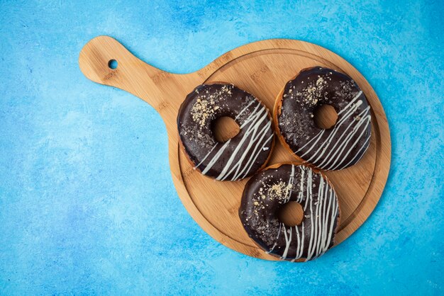 Three chocolate donuts on wooden plate and on blue background. 