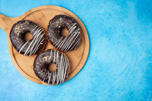 나무 접시와 파란색 배경에 3 개의 초콜릿 도넛.