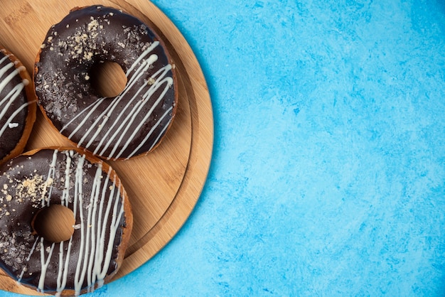 Три шоколадных пончика на деревянной тарелке и на синем фоне.