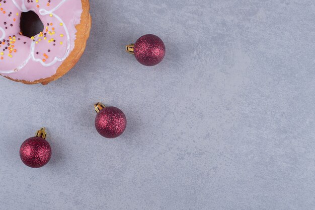 Three christmas baubles and a donut on marble surface