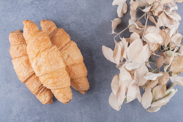 Free photo three classic french croissant with decorative leaves over grey background.