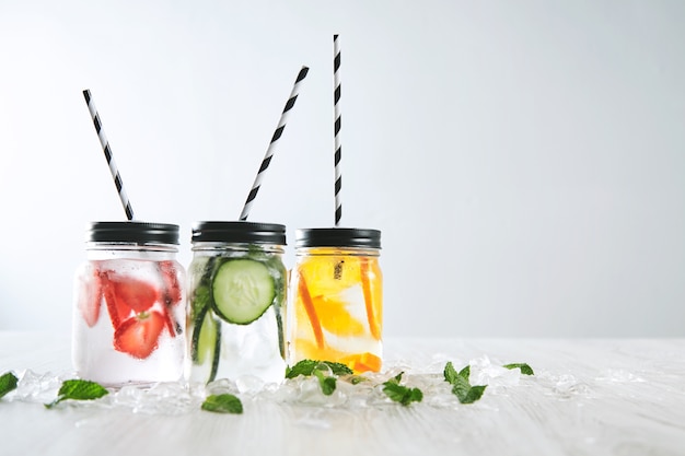 Three cold refreshment beverages and sparkling water in rustic jars with drinking straws inside