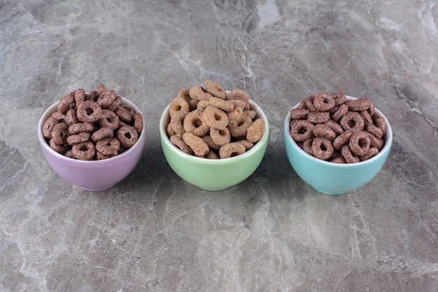 Three colorful bowls of chocolate cereal rings for breakfast . 